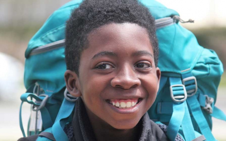 A young person wearing a backpack smiles at the camera 